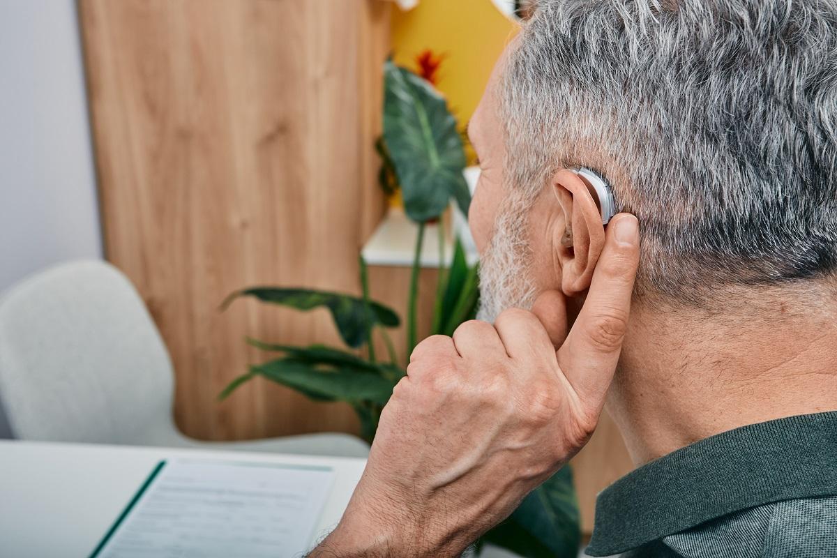 Elderly man holding his finger to his hearing aid on his ear
