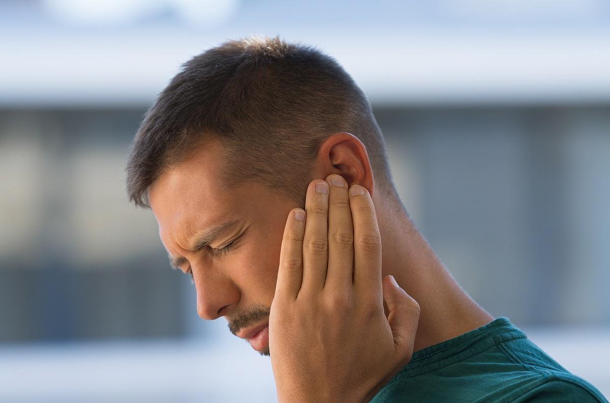 Young man with ringing in ears holding hand to his ear