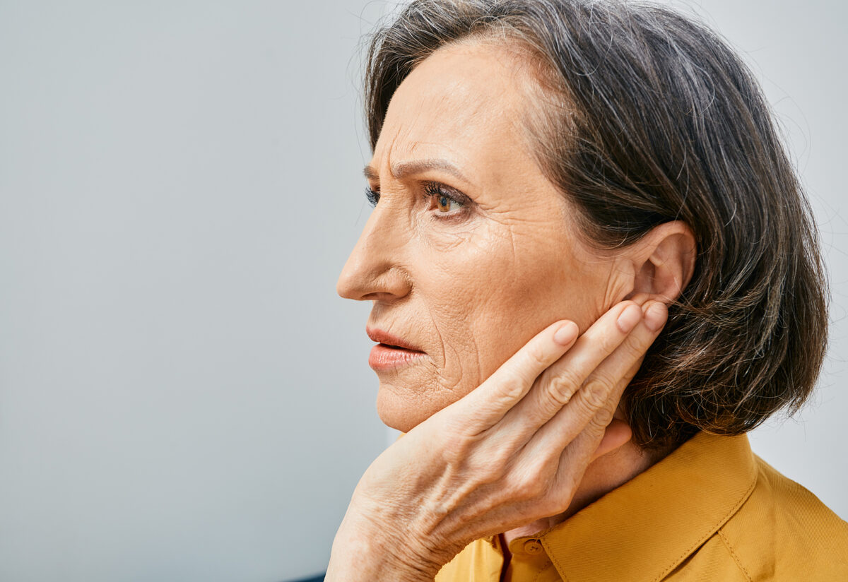 Mature woman holding her hand up to her ear with grimace on her face